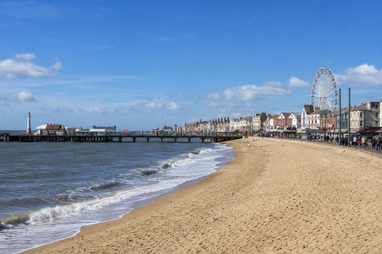 Sunny beach scene with a pier, lighthouse, Ferris wheel, and colorful seaside buildings.