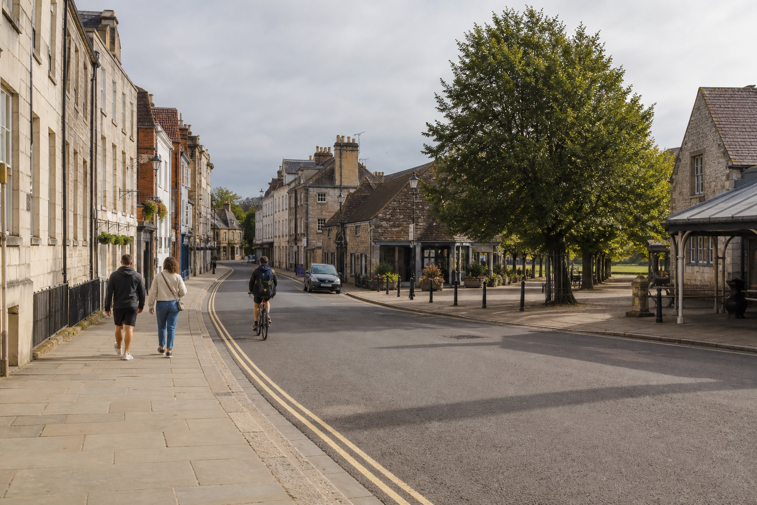 People walking and a cyclist on a quiet street lined with historic buildings and trees.