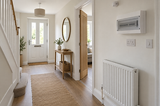 A bright, tidy hallway with wooden flooring, a console table, a round mirror, and a white front door.