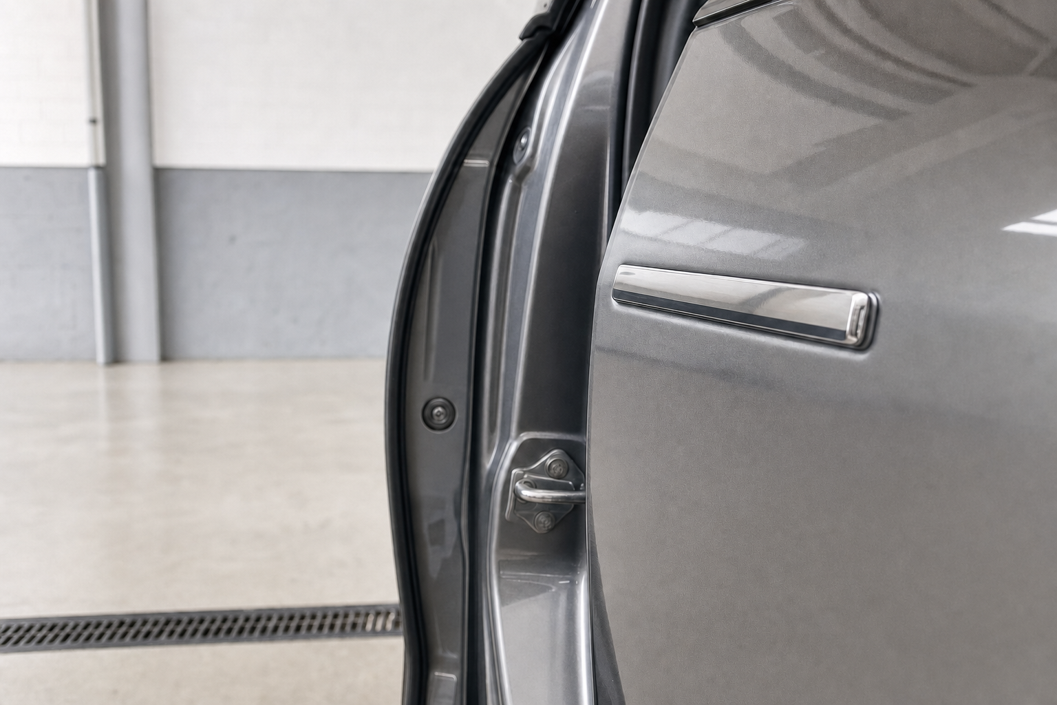 Close-up of a car door hinge and latch mechanism in a garage setting.