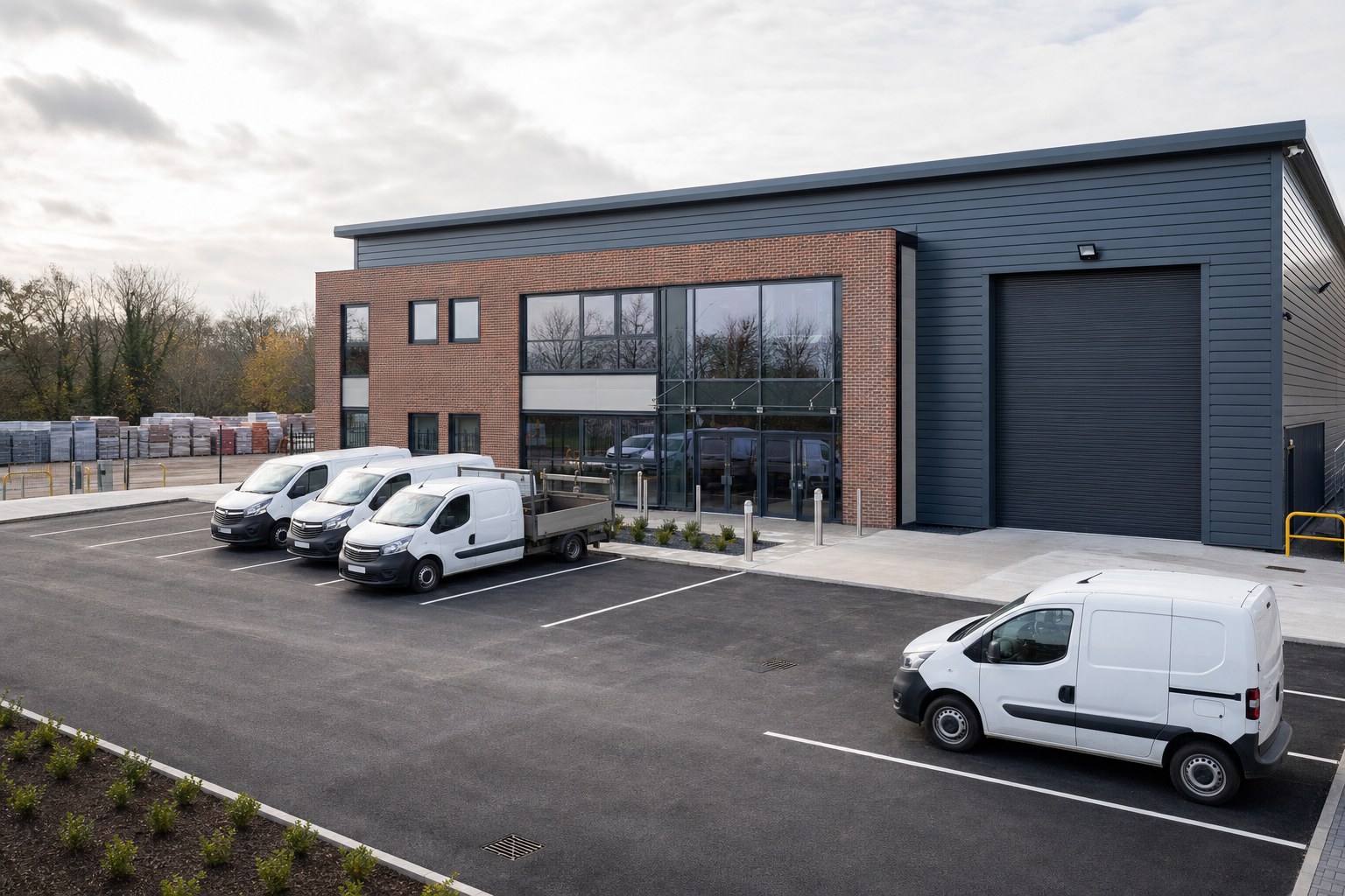 Modern industrial building with a brick facade and several white vans parked in the adjacent lot.