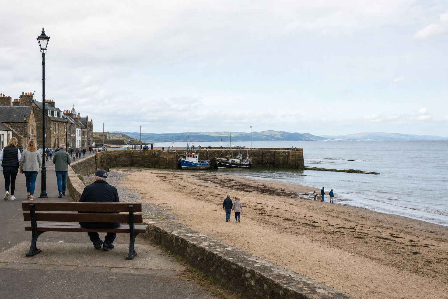 Seaside promenade with people walking along the shore, boats moored at a harbour, and distant hills on the horizon.