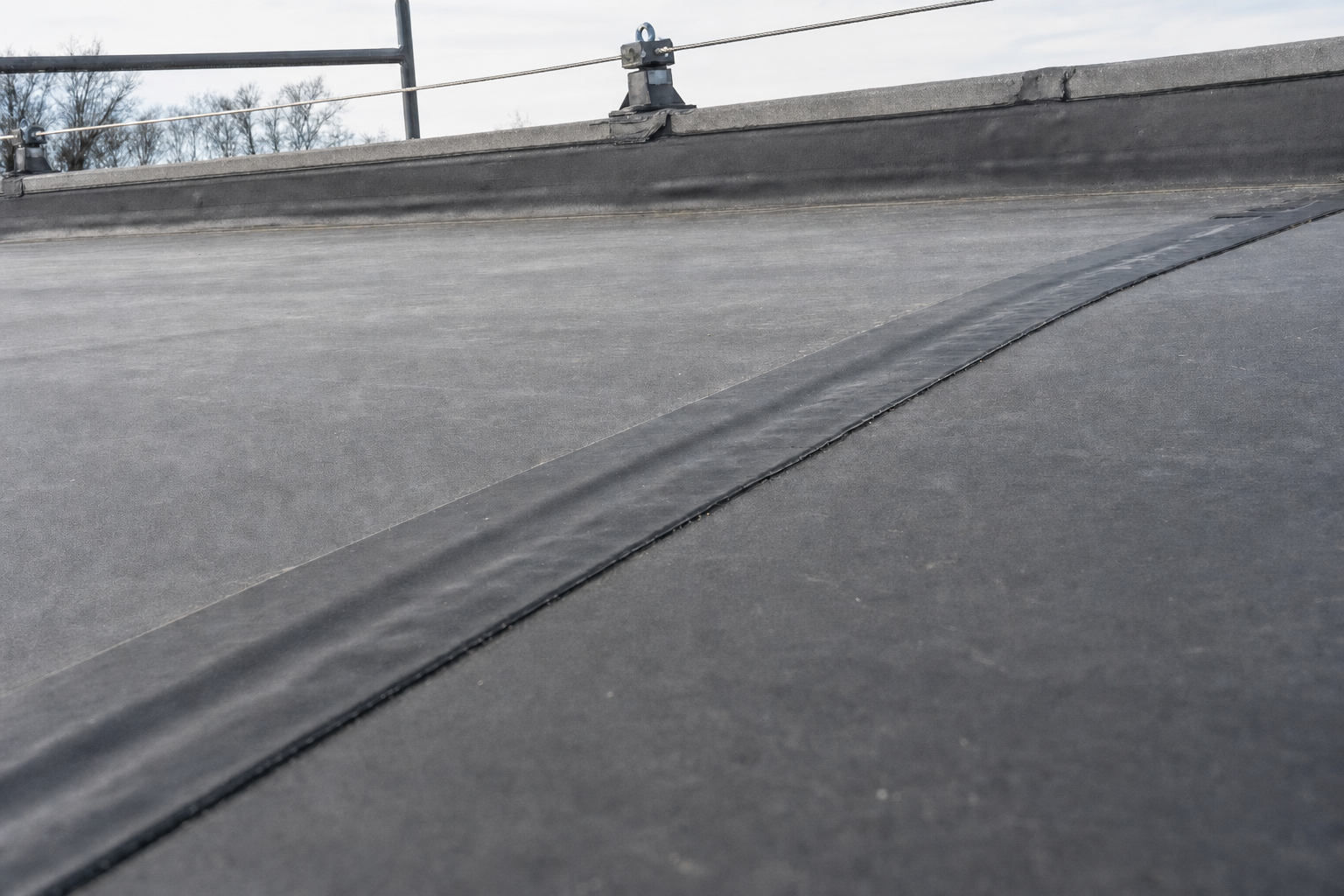 Flat rubber membrane roof with safety railing and trees in the background.