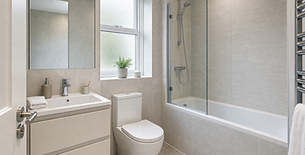 Modern bathroom with a sleek basin, large mirror, glass shower, and a small potted plant by the window.