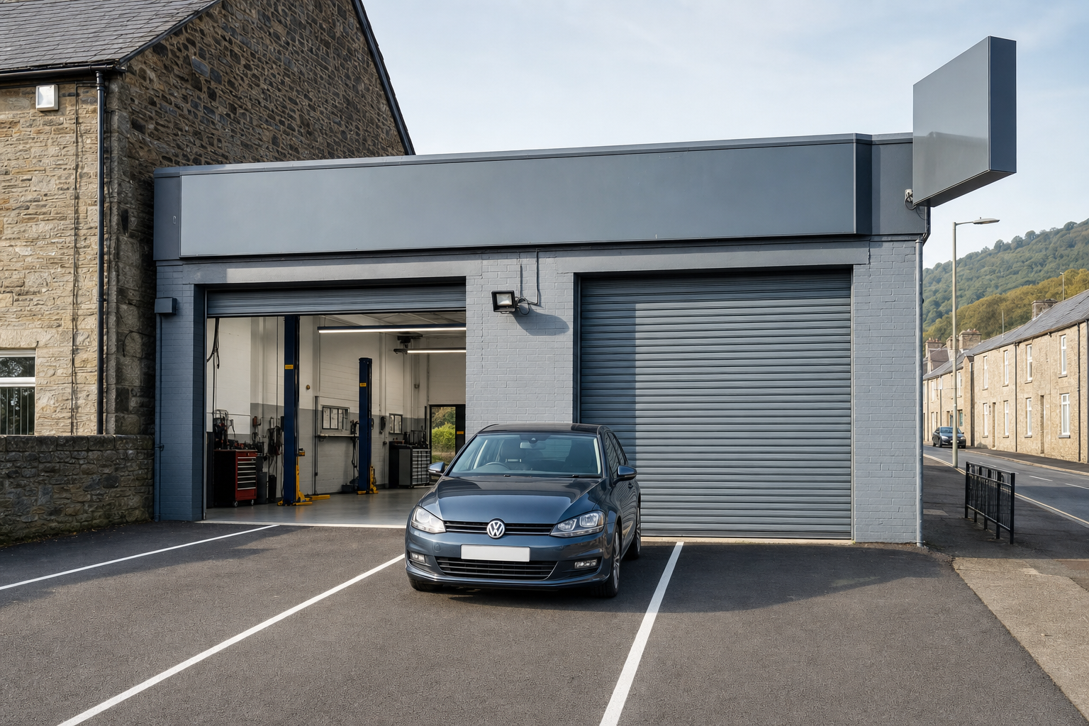 Car parked outside a closed garage with open workshop, next to a stone building on a quiet street.