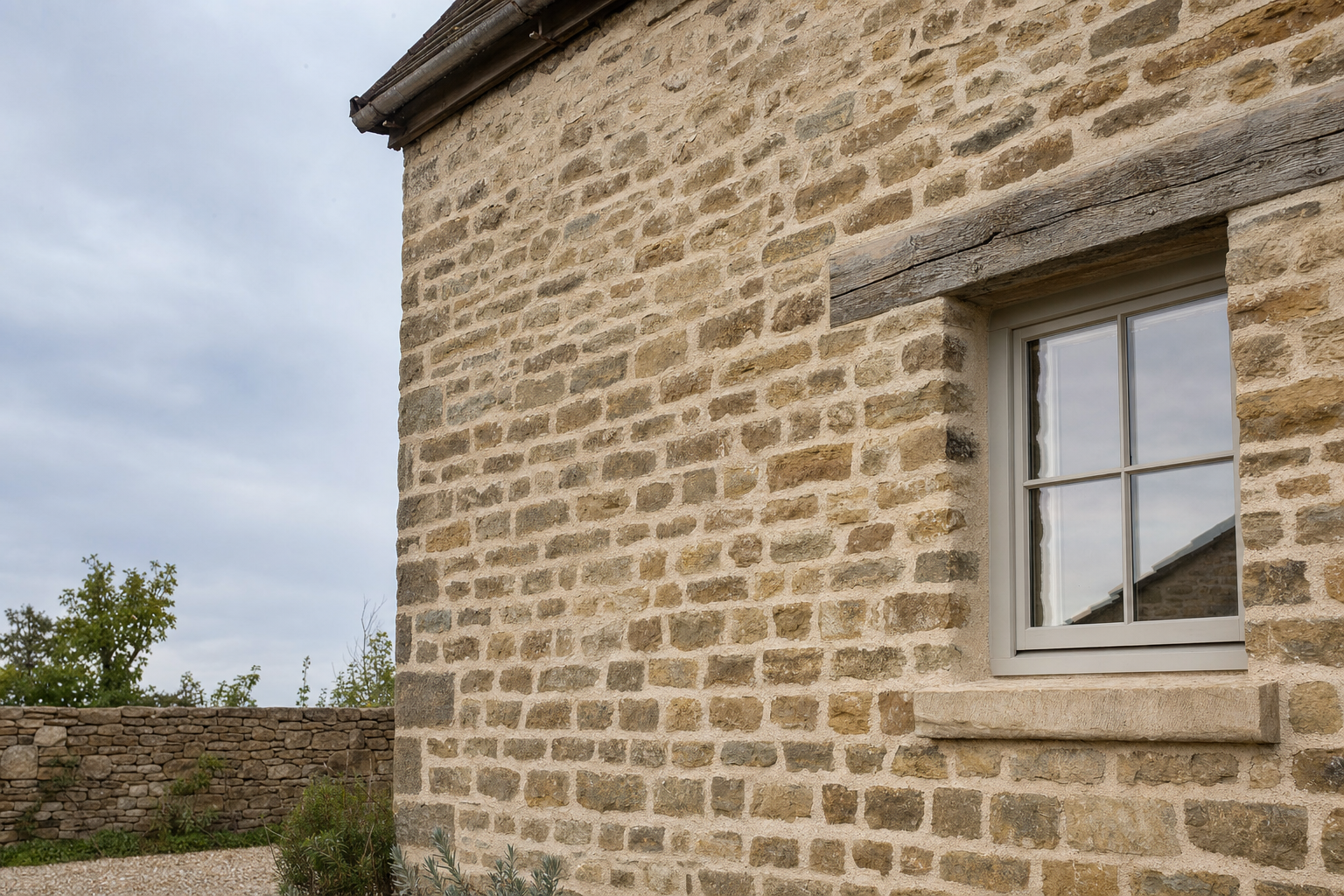 Stone cottage wall with a single window, surrounded by a garden and a stone fence.
