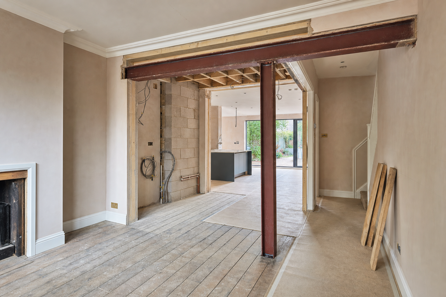 A partially renovated interior with exposed beams and walls, leading to a modern kitchen and garden view.