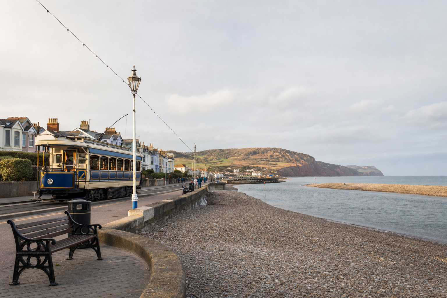 Historic tram passing along a coastal road with houses and cliffs in the background.