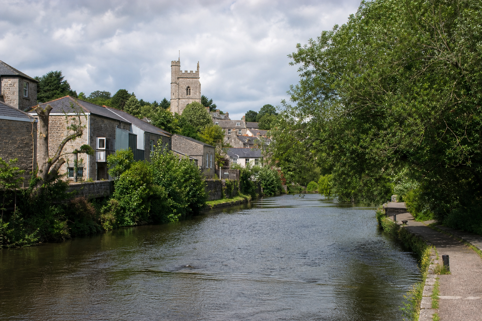 A tranquil river scene with stone buildings, lush greenery, and a church tower in the background.