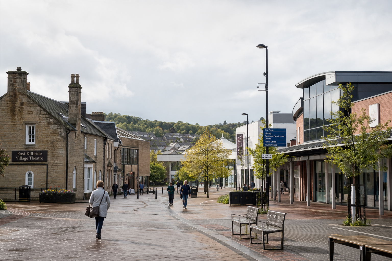 People walking along a modern street with shops and historic buildings under a cloudy sky.