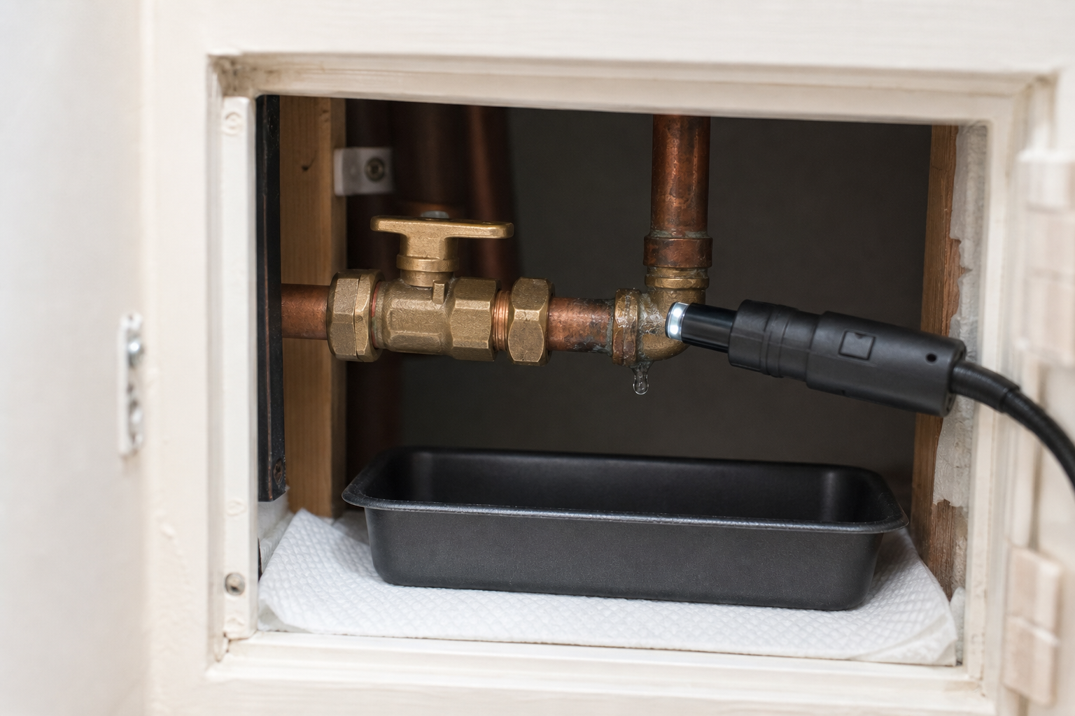 Plumbing pipe with a small drip connected to a leak detection sensor over a drip tray.