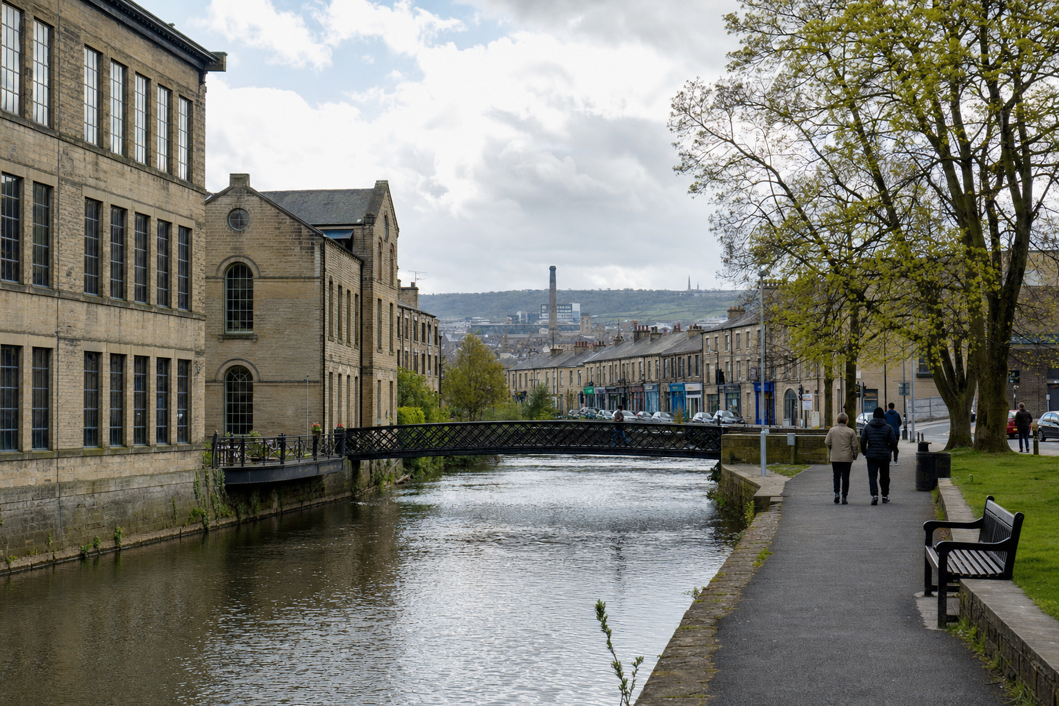 Canal-side walkway with people strolling, historic buildings, and a bridge under a cloudy sky.
