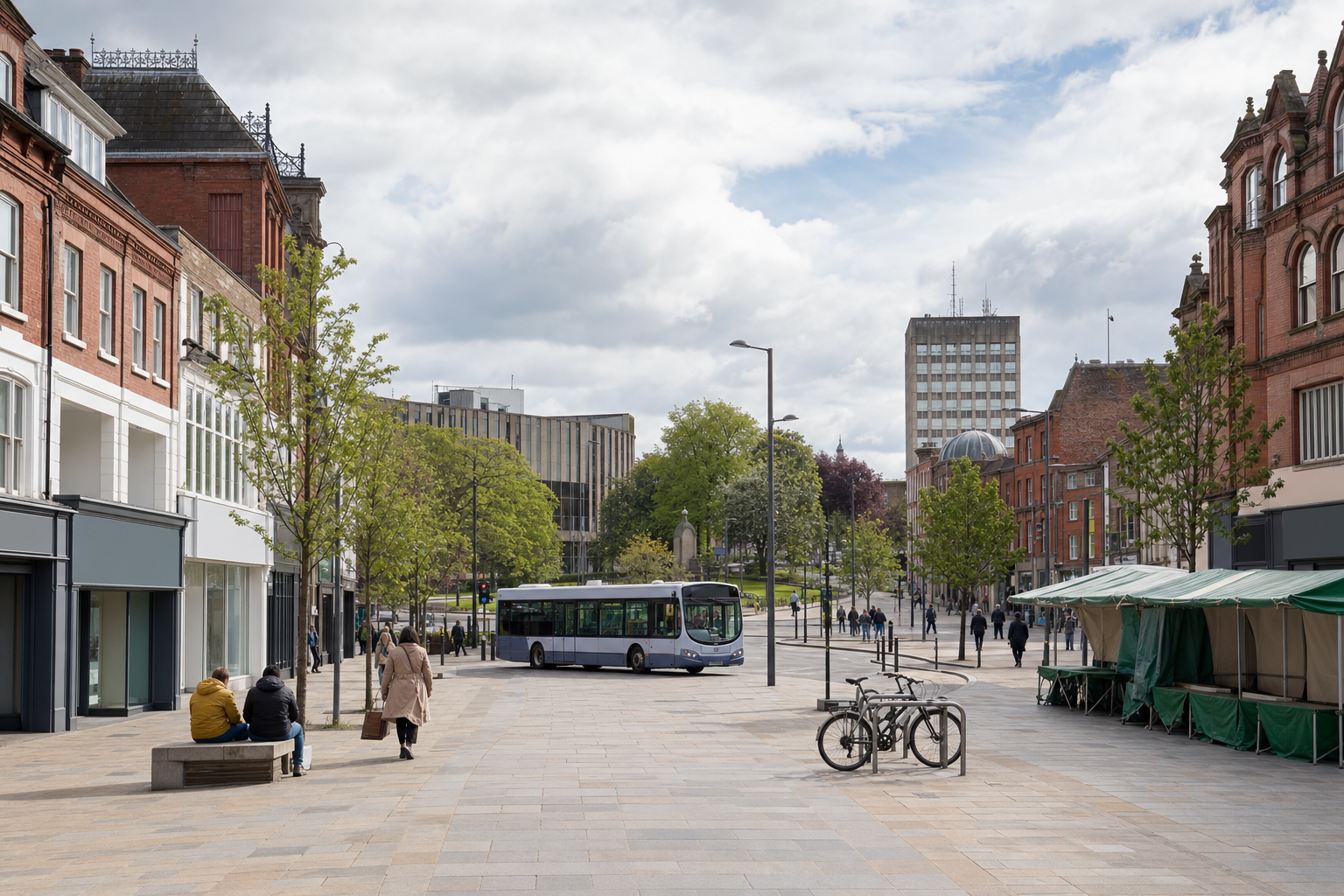 A bus drives through an urban street lined with shops and trees, with people walking and bicycles parked nearby.