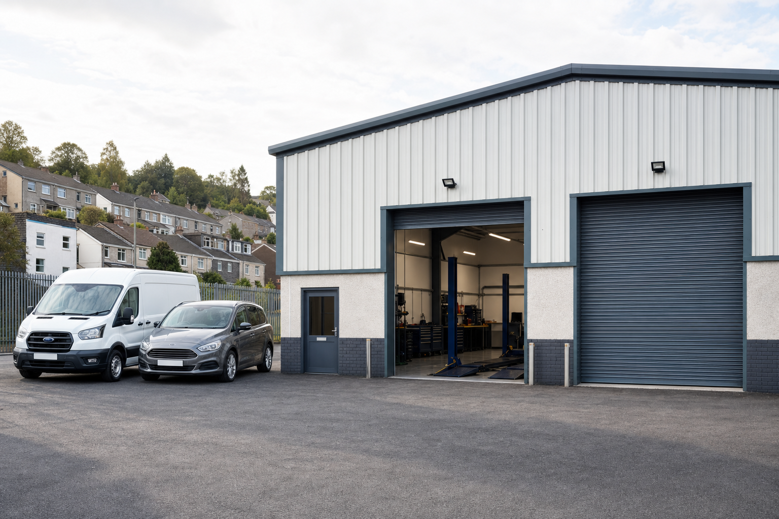 A modern industrial garage with open doors revealing vehicle lifts, adjacent to a white van and grey car in the parking area.