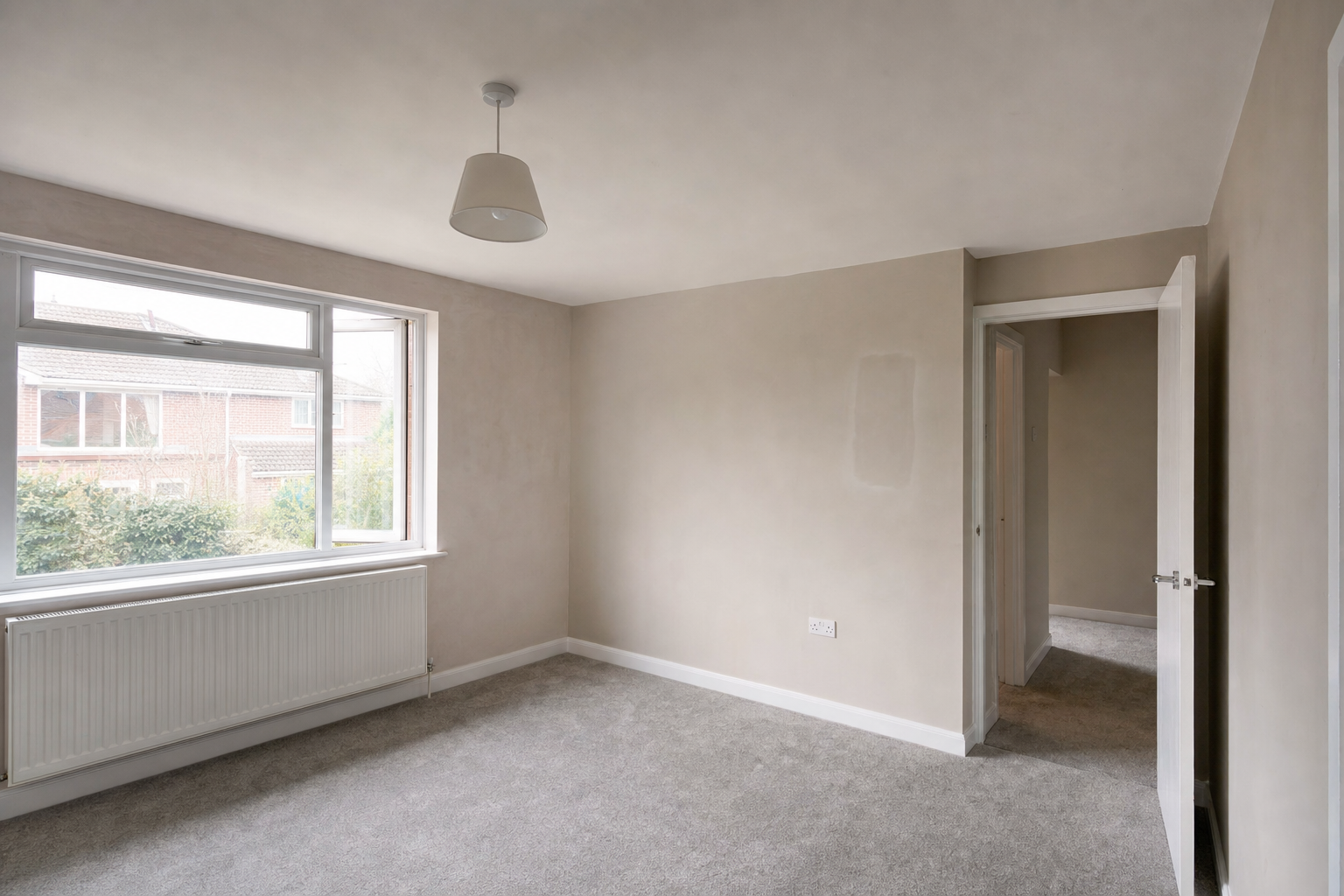 Empty room with beige walls, grey carpet, a large window, and an open door leading to a hallway.