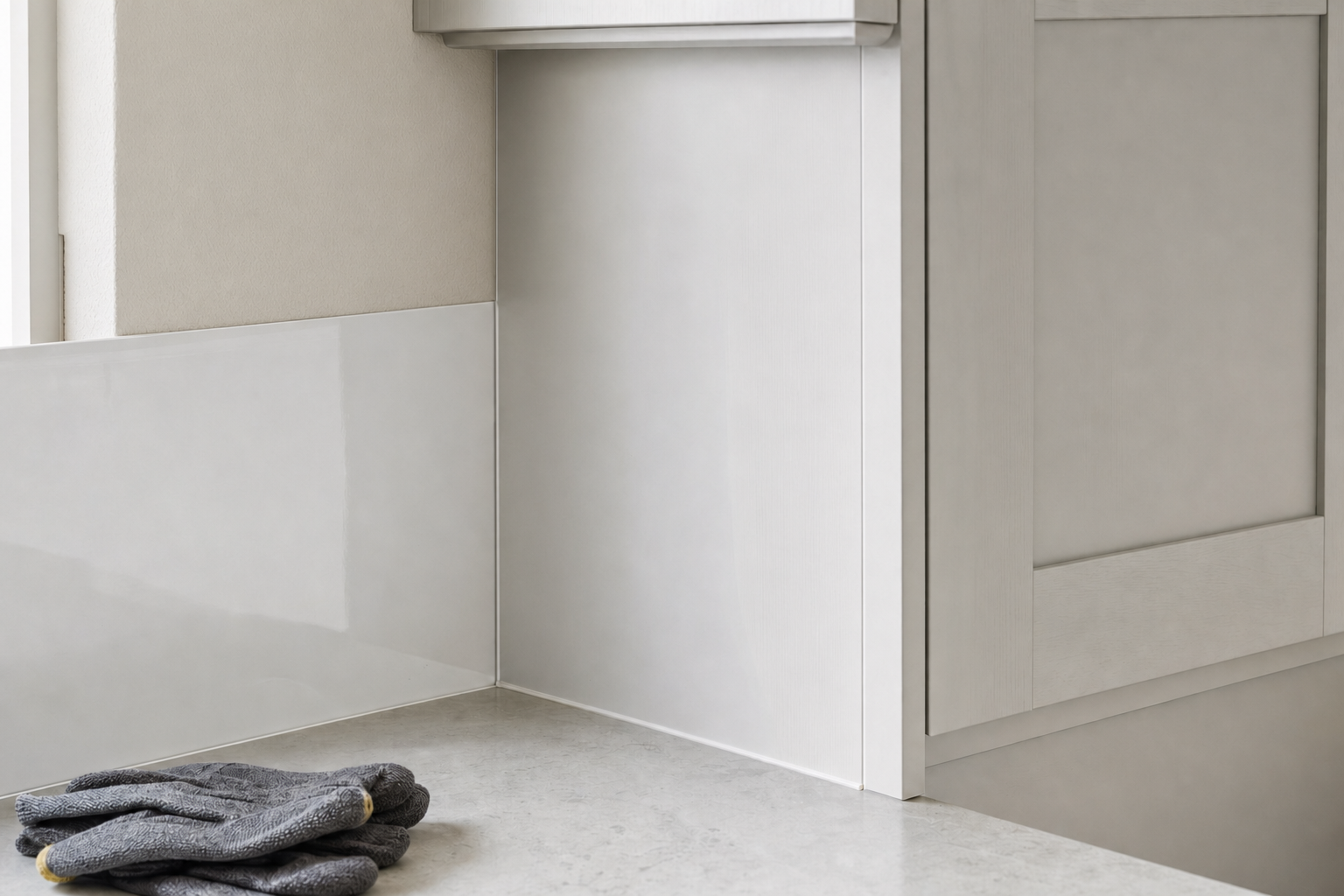 A minimalist kitchen corner with white cabinets and a grey worktop, featuring folded oven gloves.