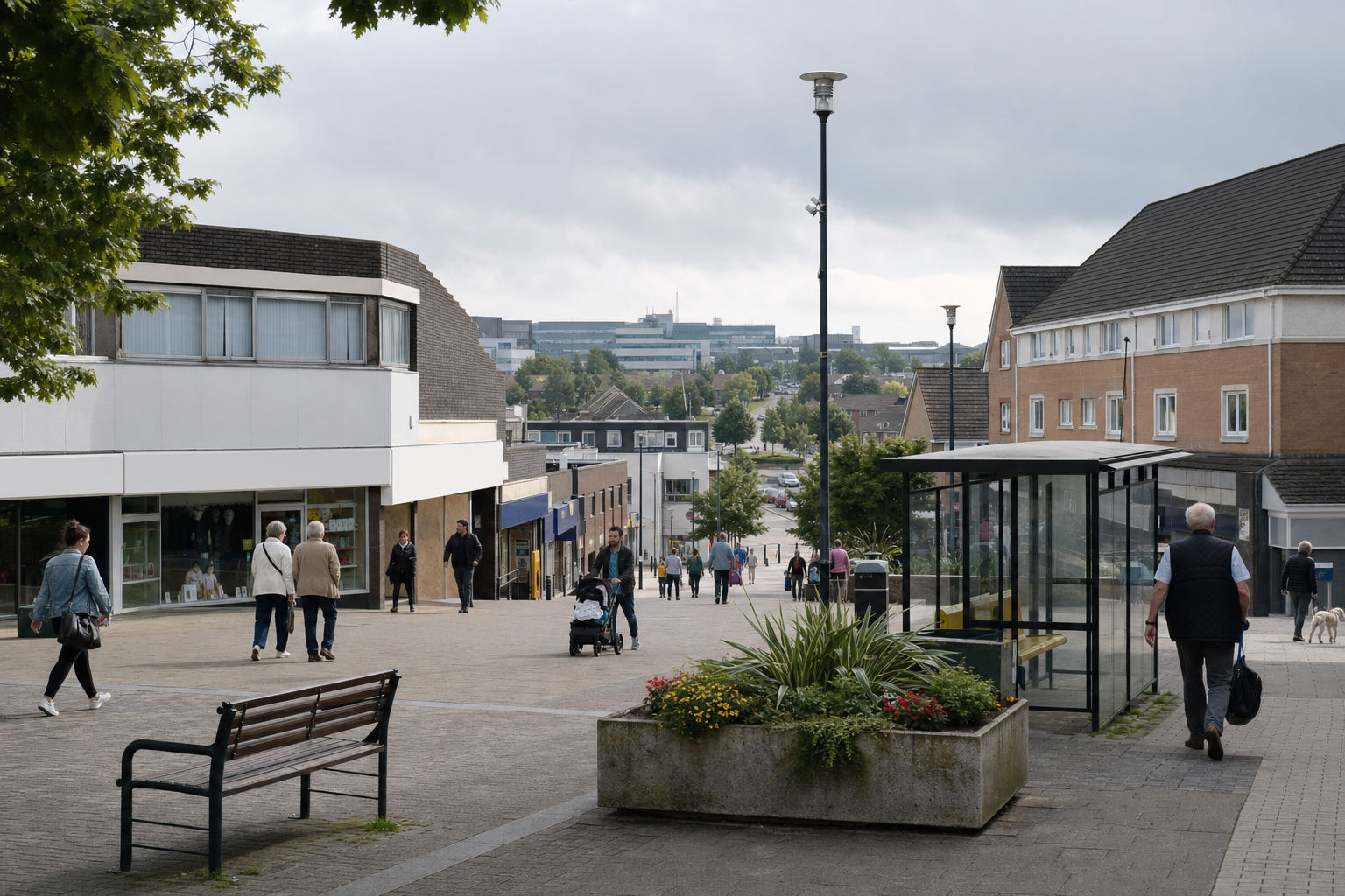 A bustling town centre with people walking, a bus shelter, and shopfronts under a cloudy sky.