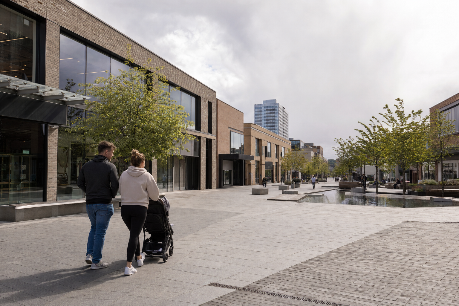 A couple strolls with a pram through a modern urban street lined with trees and contemporary buildings.