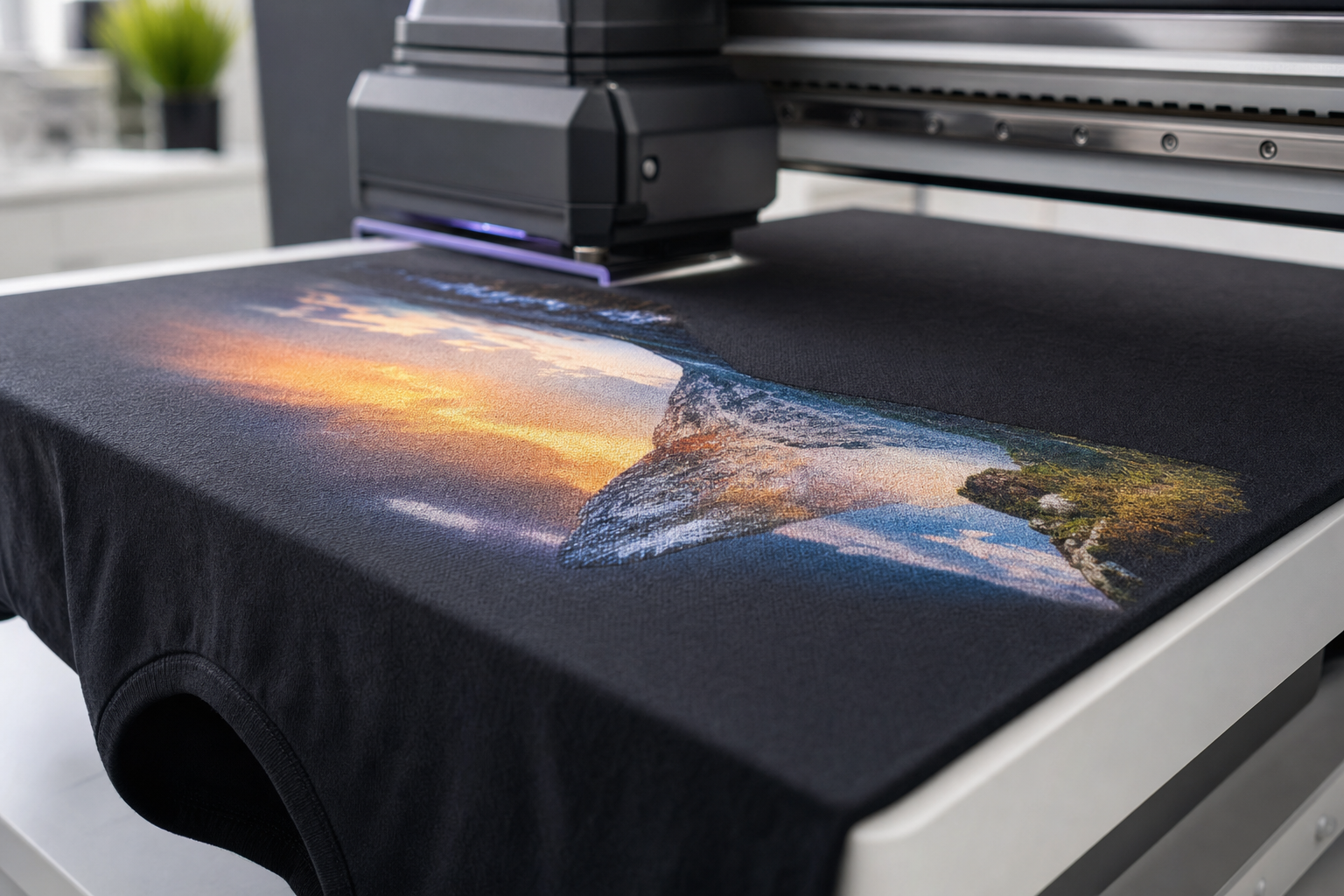 A digital printer applies a vivid landscape image onto a black T-shirt in a modern setting.