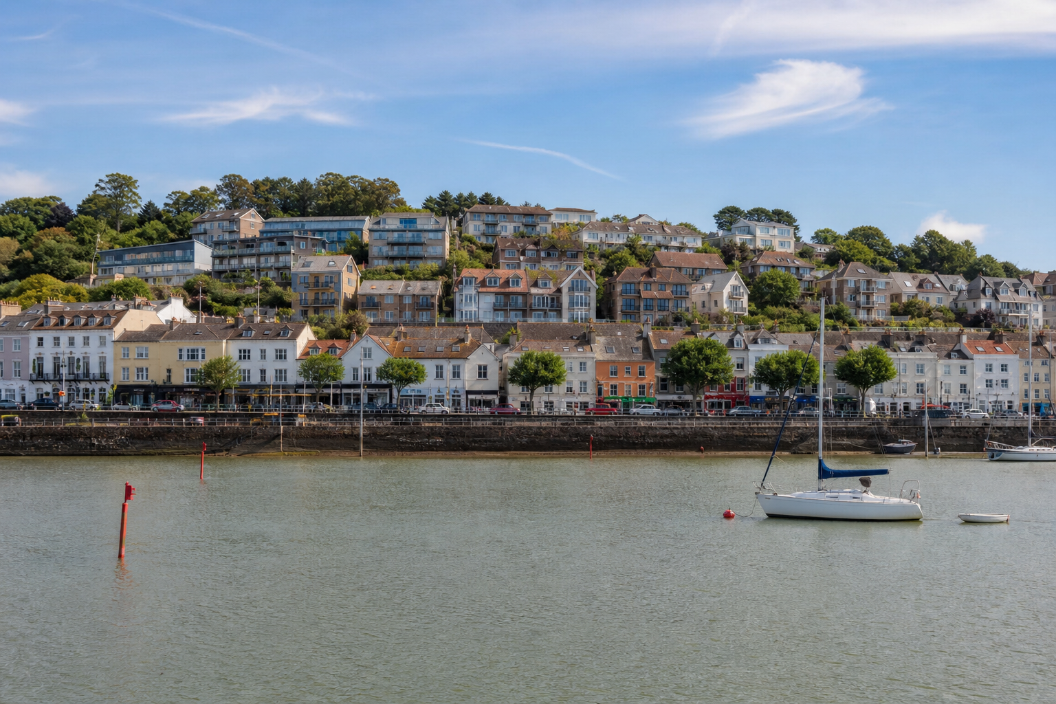 Sailboats anchored near a charming seaside town with colorful hillside houses.