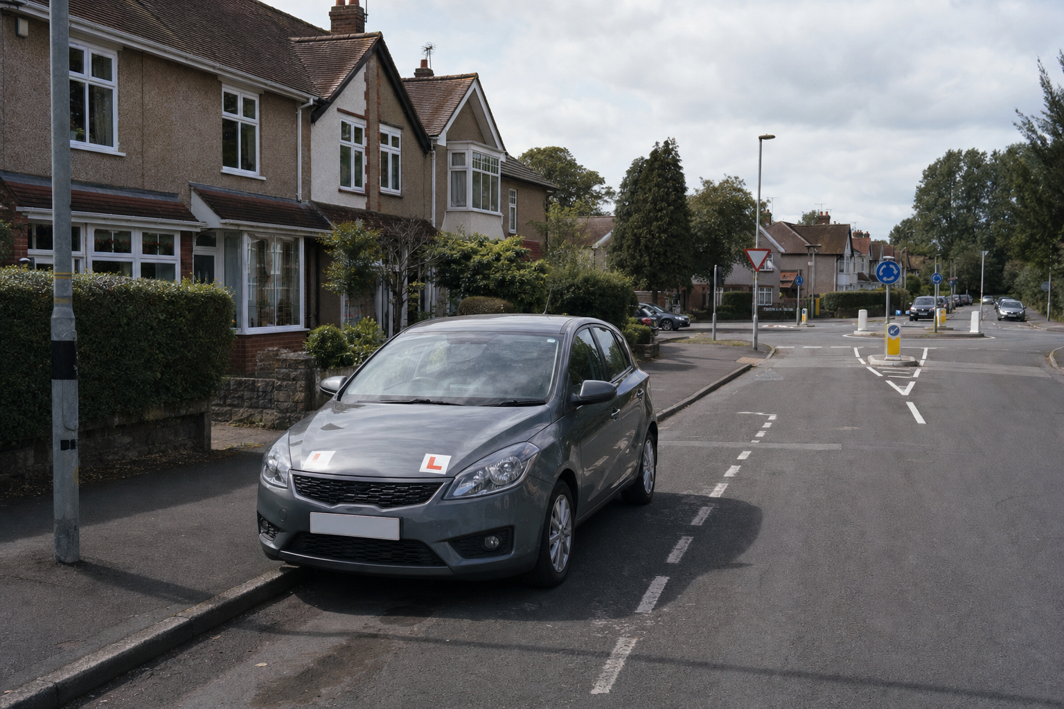 Grey car with L-plates parked on a residential street near a mini roundabout.