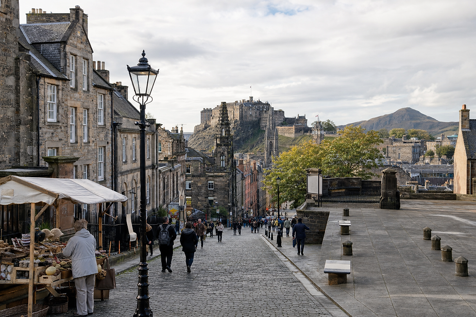 Edinburgh Castle overlooks a cobblestone street bustling with people and a small outdoor market.