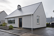 Modern grey bungalow with a black front door and a small garden, situated on a wet street.
