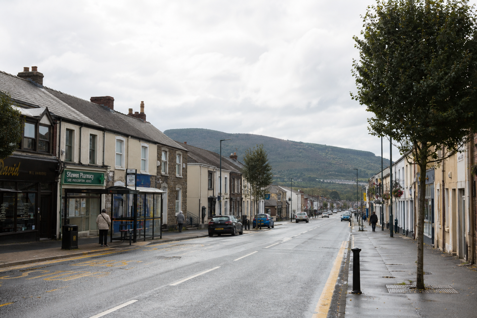 A quiet street scene with terraced shops and a distant hill under a cloudy sky.