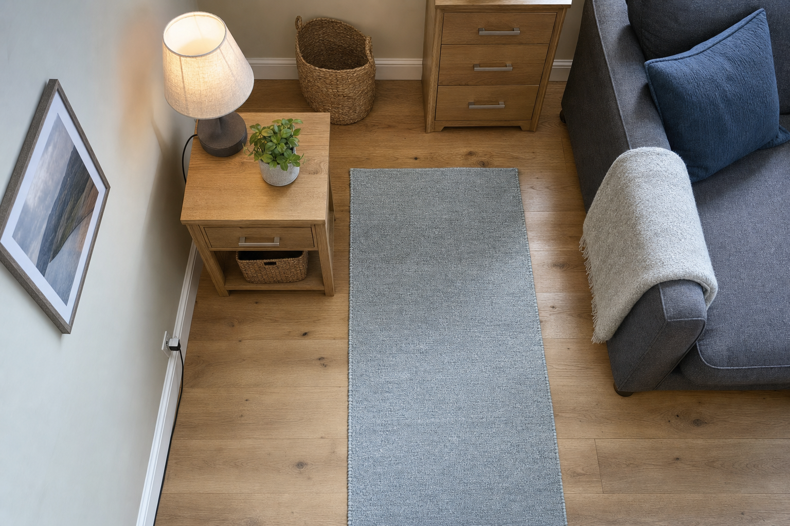 Cosy living room with wooden furniture, a grey sofa, a light blue rug, and a lamp on a side table.