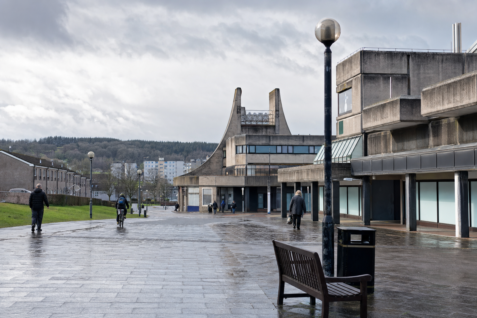 People walk and cycle through a damp, modern architectural square with a distinctive concrete building.