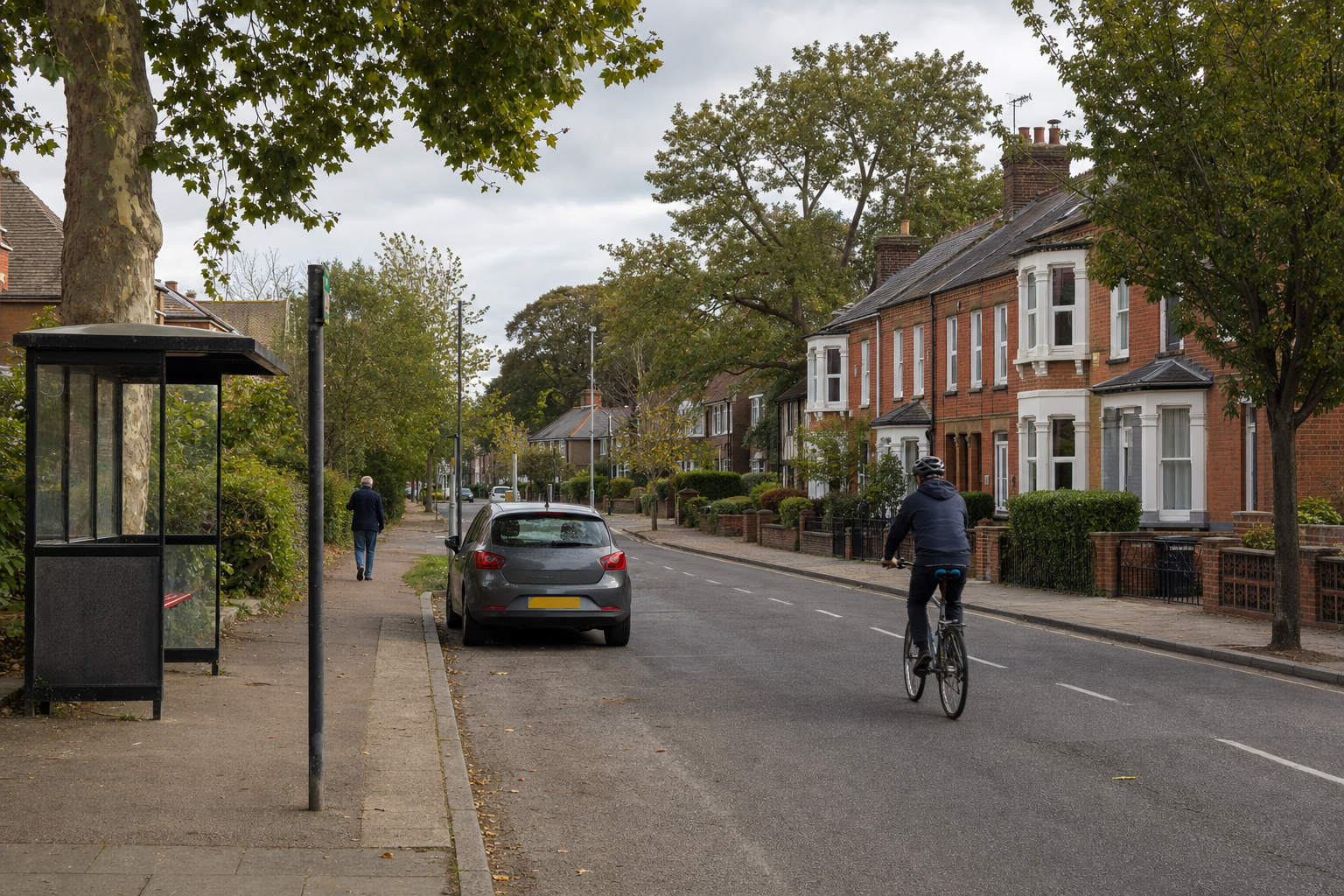 Cyclist riding down a quiet suburban street lined with brick houses and a bus stop.