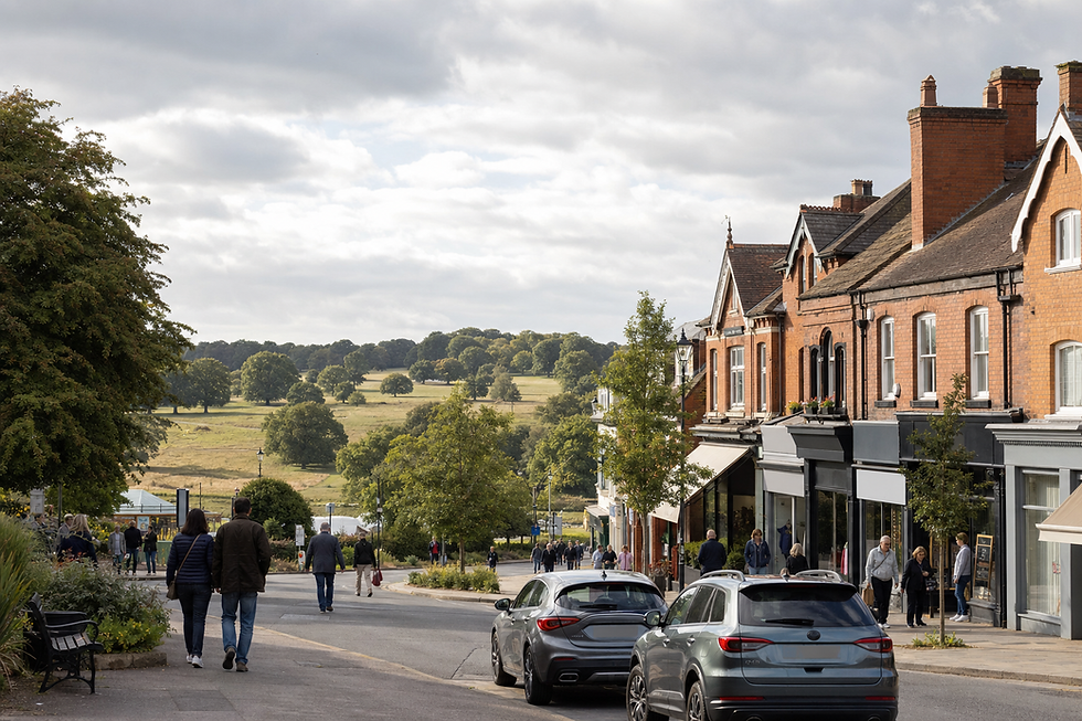 A quiet street with red-brick buildings leads to a scenic countryside view under a partly cloudy sky.