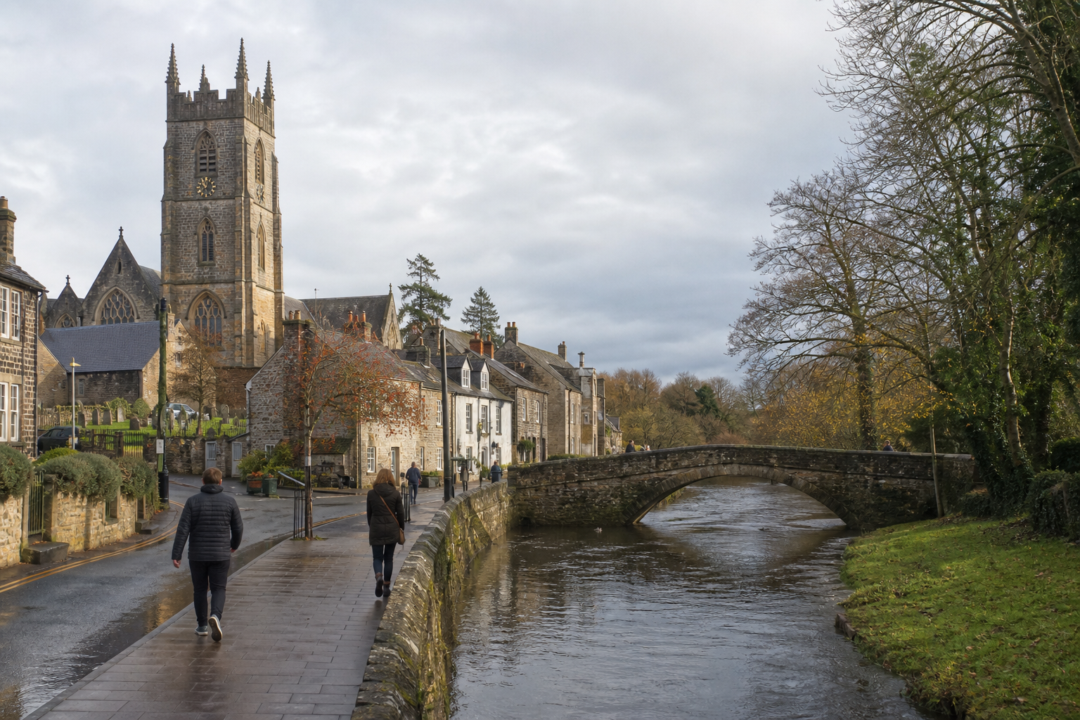 A historic stone church and village buildings sit beside a river, with people walking along a riverside path and stone bridge.