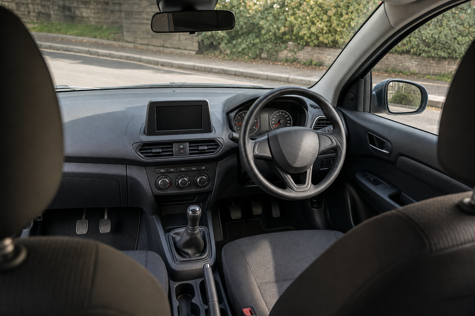 Interior view of a car showing the dashboard, steering wheel, and manual gear lever with a street view outside.