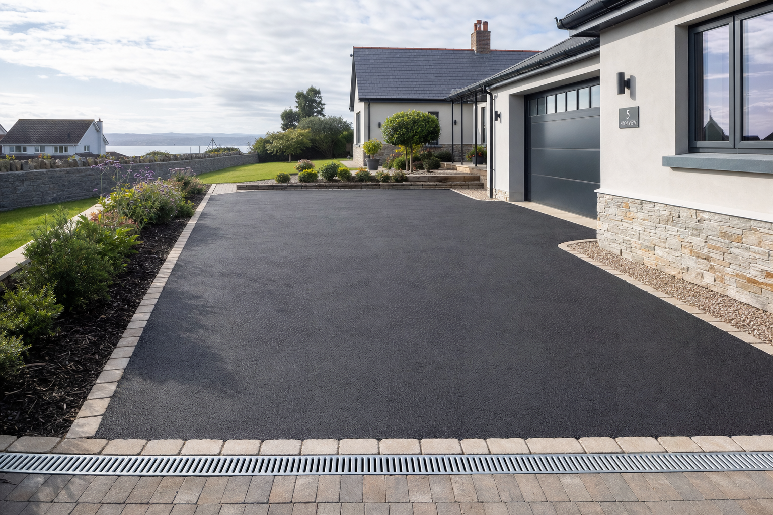 Modern house with a freshly paved driveway and well-maintained garden under a partly cloudy sky.