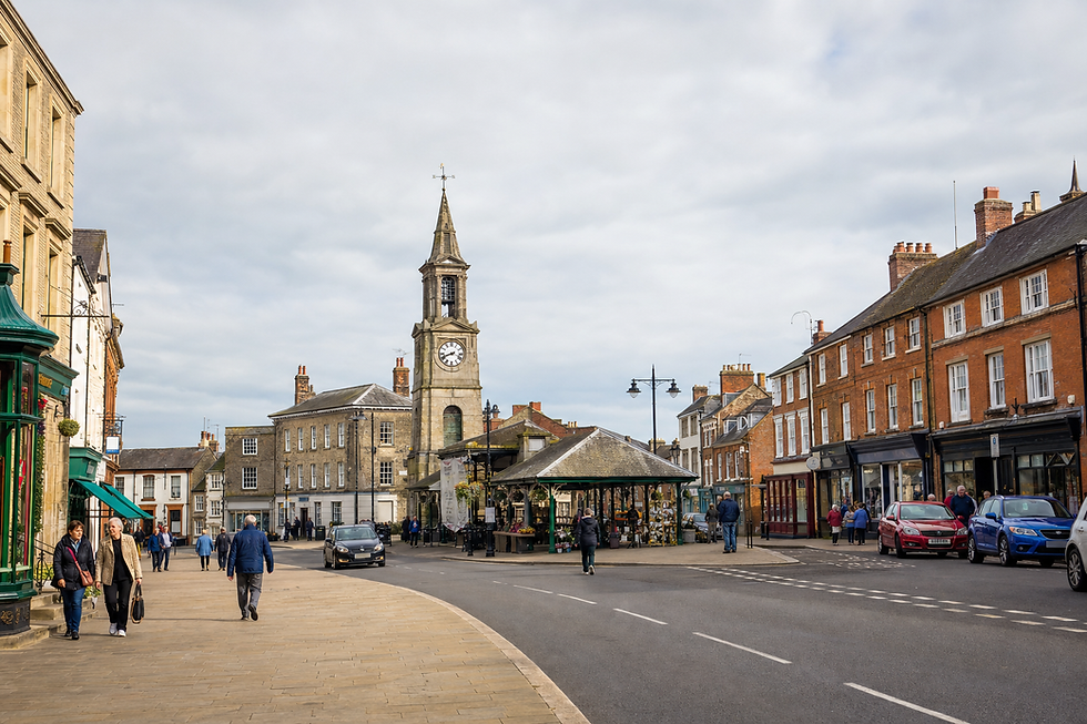 A bustling market square with historic buildings and a clock tower in a charming English town.