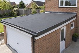 A flat garage roof with a black edge trim next to a brick house in a residential garden setting.