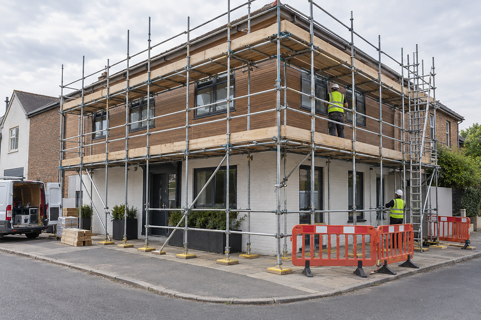 Workers in high-visibility vests on scaffolding renovating a corner building with wooden and brick exterior.