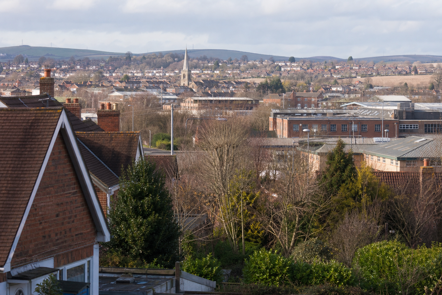 A quaint townscape with rooftops, trees, and a church spire in the background.