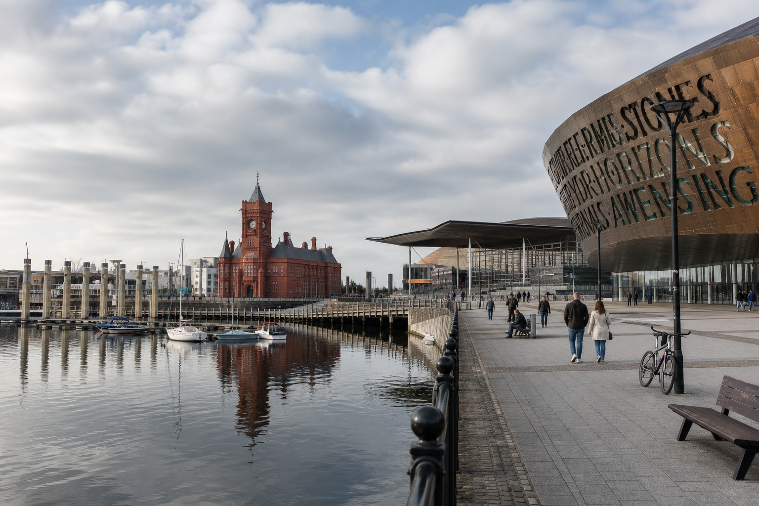 Cardiff Bay with the red Pierhead Building, Wales Millennium Centre, and boats reflected in the water under a cloudy sky.