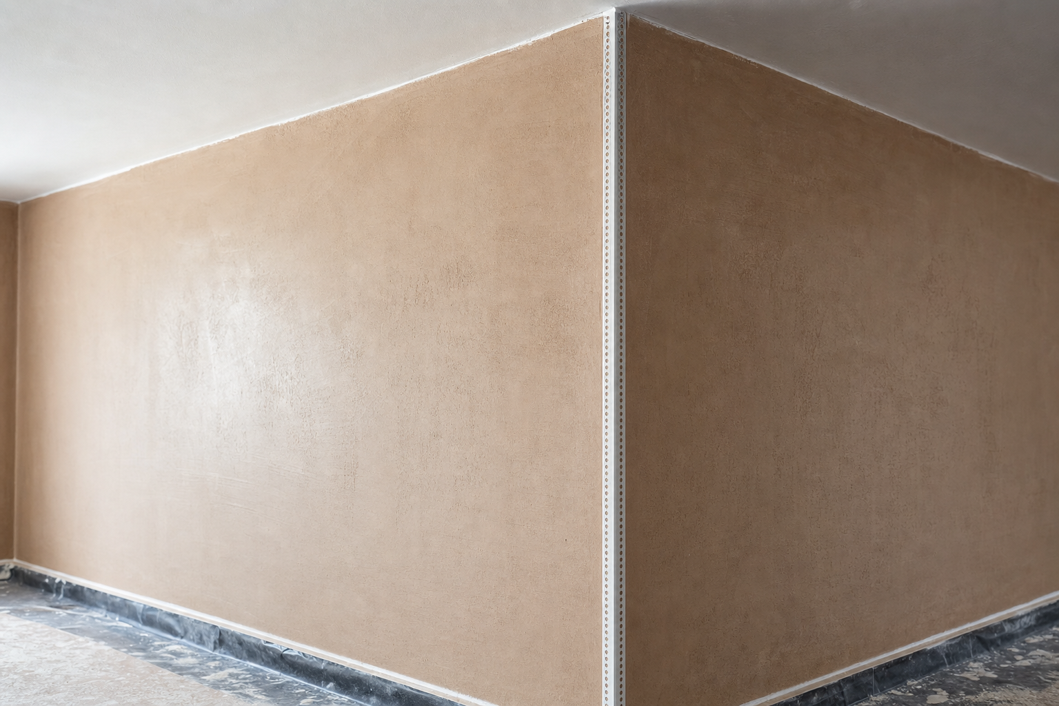 Corner of an unfinished room with freshly plastered beige walls and a rough concrete floor.