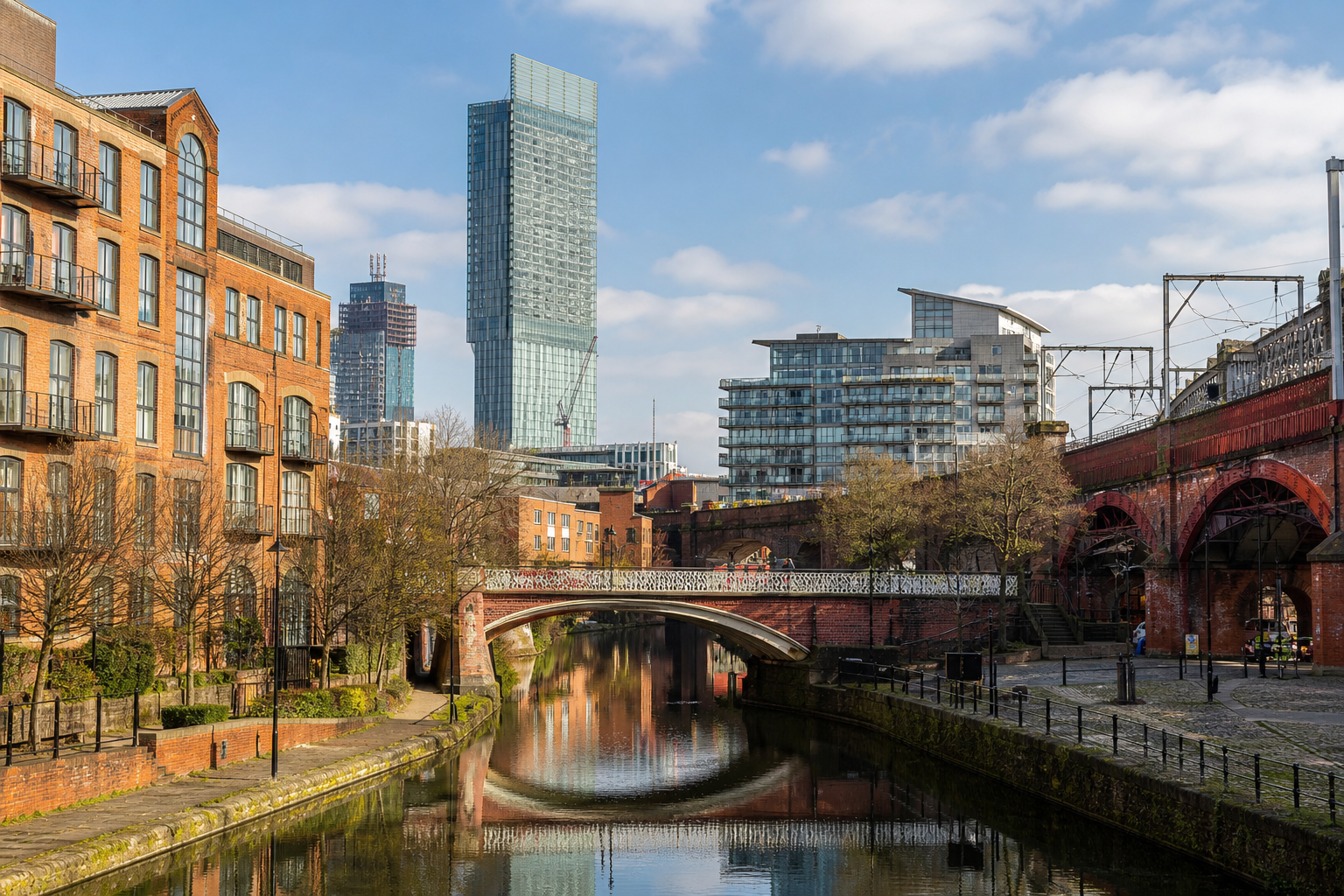Urban canal scene with a mix of brick buildings, a modern high-rise, and a bridge under a blue sky.
