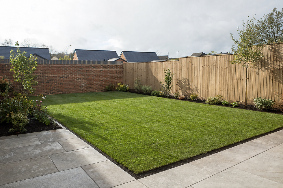 A neatly trimmed garden with a lush green lawn, paved patio, and fenced surroundings on a partly cloudy day.