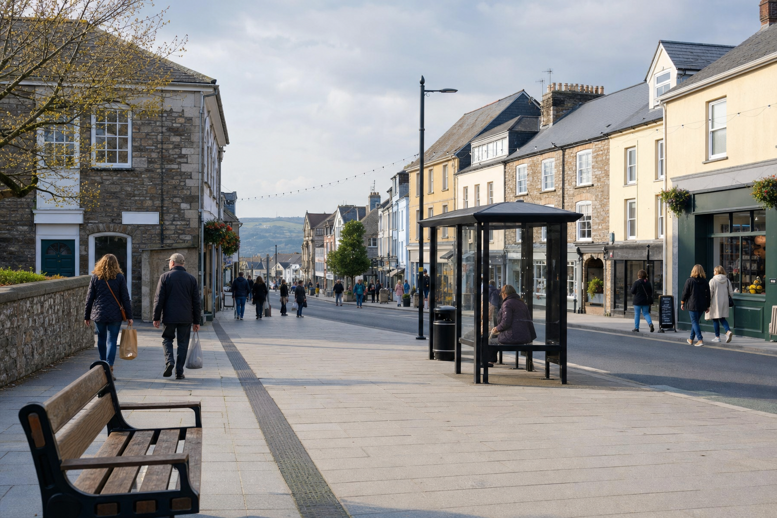 People walking along a lively, pedestrian-friendly street with shops, benches, and a bus stop on a clear day.