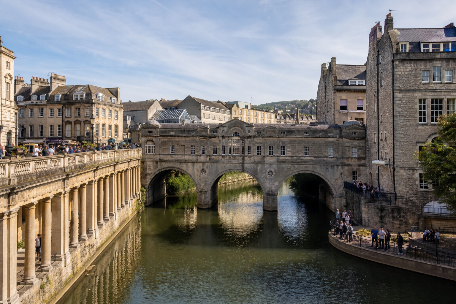 Historic stone bridge with arched walkways spanning a calm river, surrounded by classical architecture.