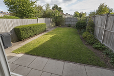 A neatly maintained back garden with a paved patio, grass lawn, and wooden fencing on a sunny day.