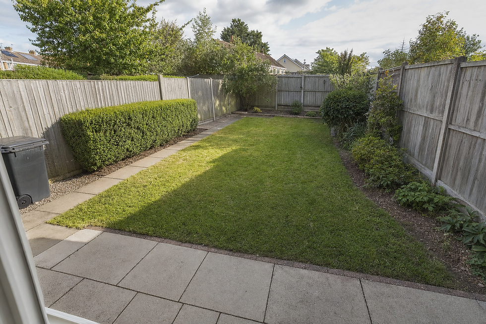 A neatly maintained back garden with a paved patio, grass lawn, and wooden fencing on a sunny day.