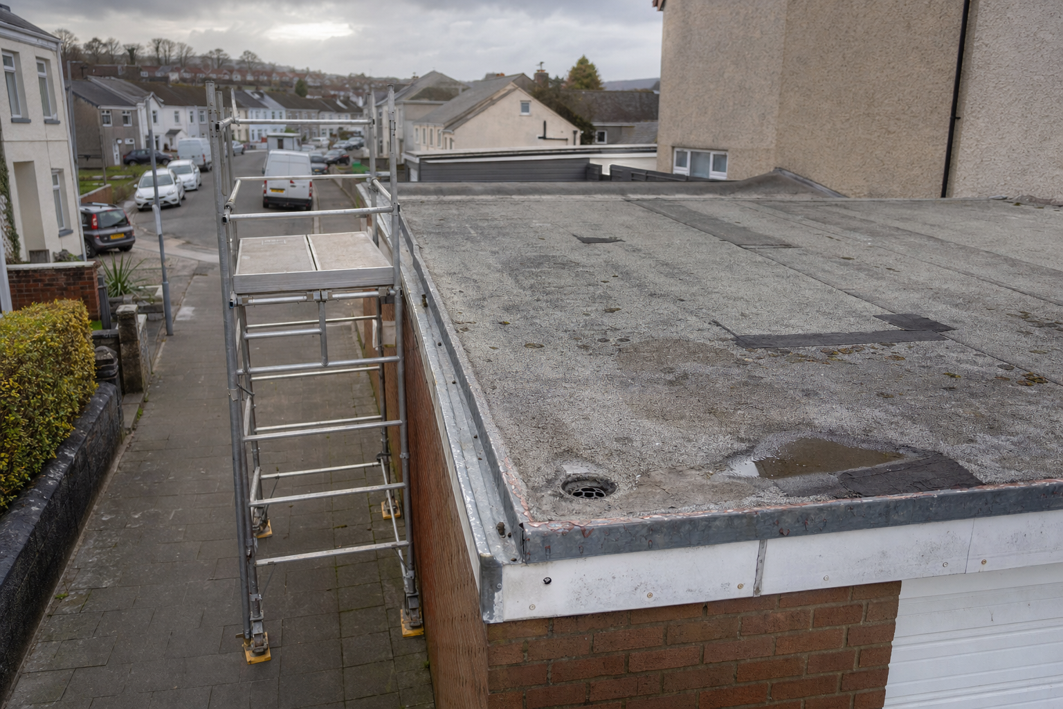 Scaffolding set up next to a flat garage roof in a residential street with overcast skies.