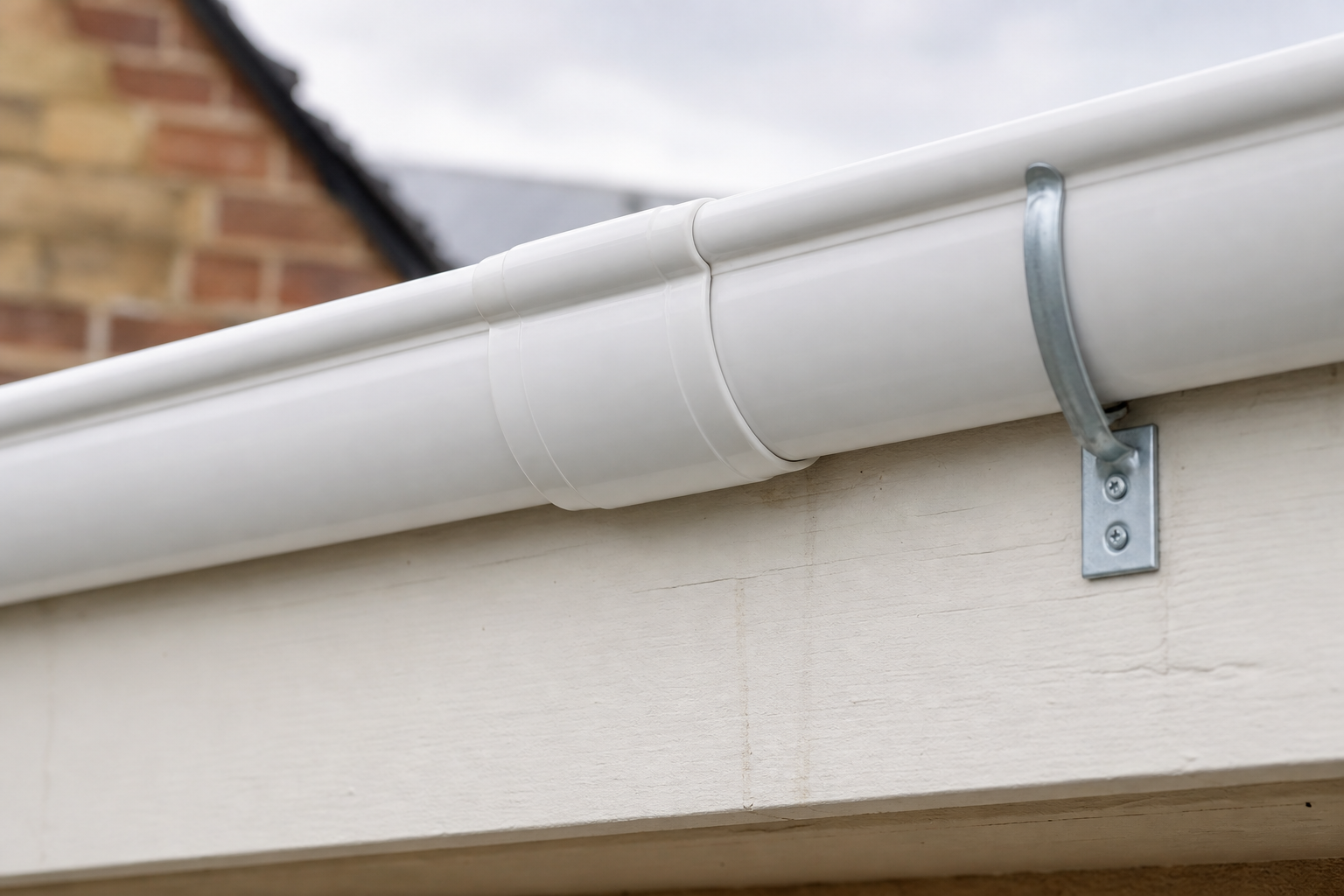 White uPVC guttering fixed to the fascia of a house, with a brick wall background.