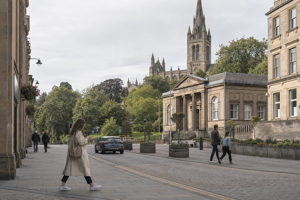 A person walks past the Carnegie Library and trees with a church spire visible in the background.